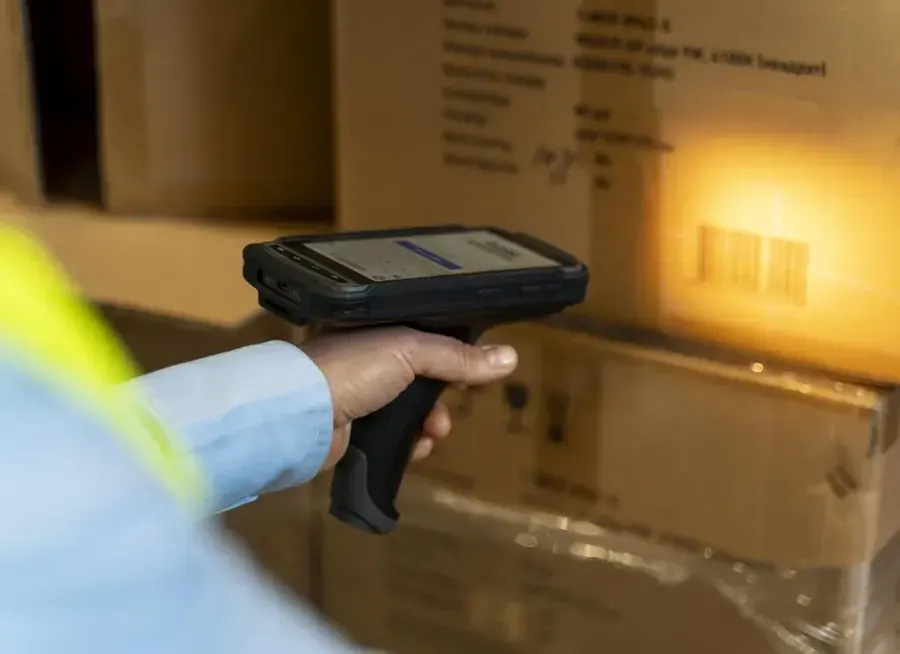 Hand holding a rugged barcode scanner aimed at a carton label