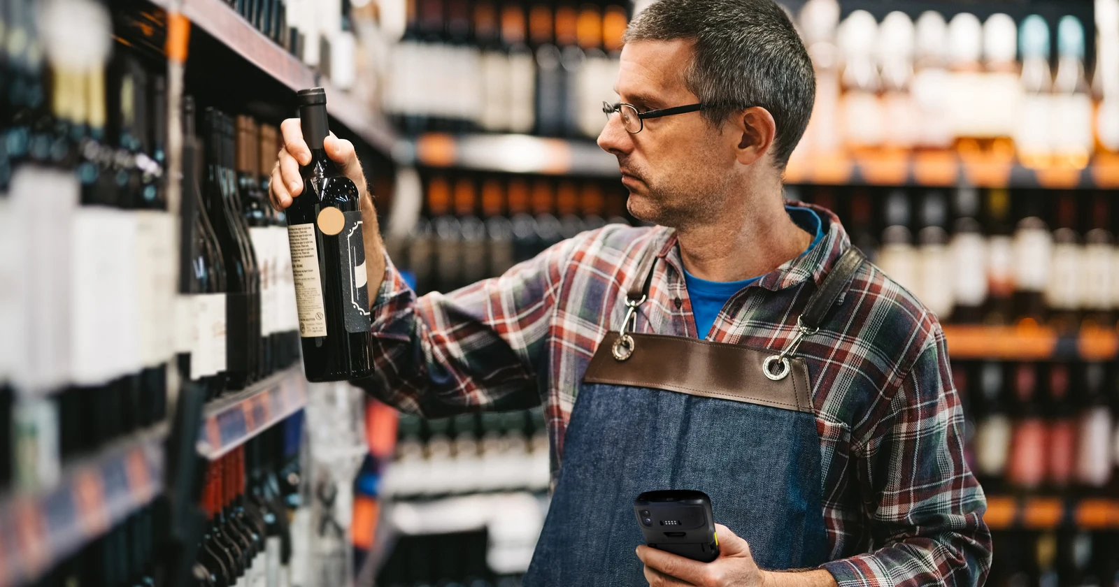 Retail employee using a handheld computer among wine shelves