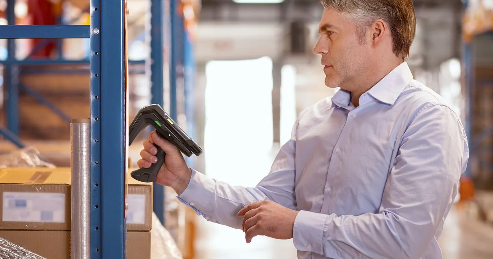 Warehouse employee scanning a carton barcode beside racking.